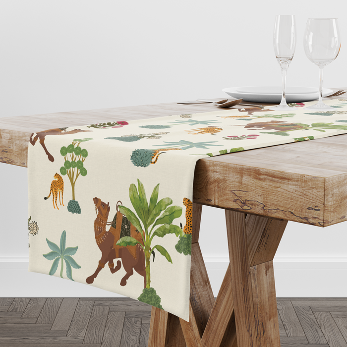Cream table runner with camel, leopard, and palm-tree motifs, styled with wine glasses and place settings