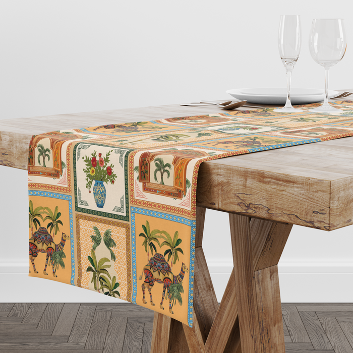 Checkered table runner with camel, palm-tree, jharokha-window, and floral vase motifs, styled with wine glasses and place settings