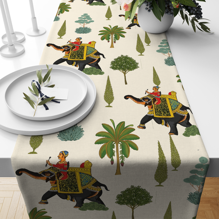 Cream table runner with decorated royal elephants, riders, and tree motifs, styled on a wooden dining table
