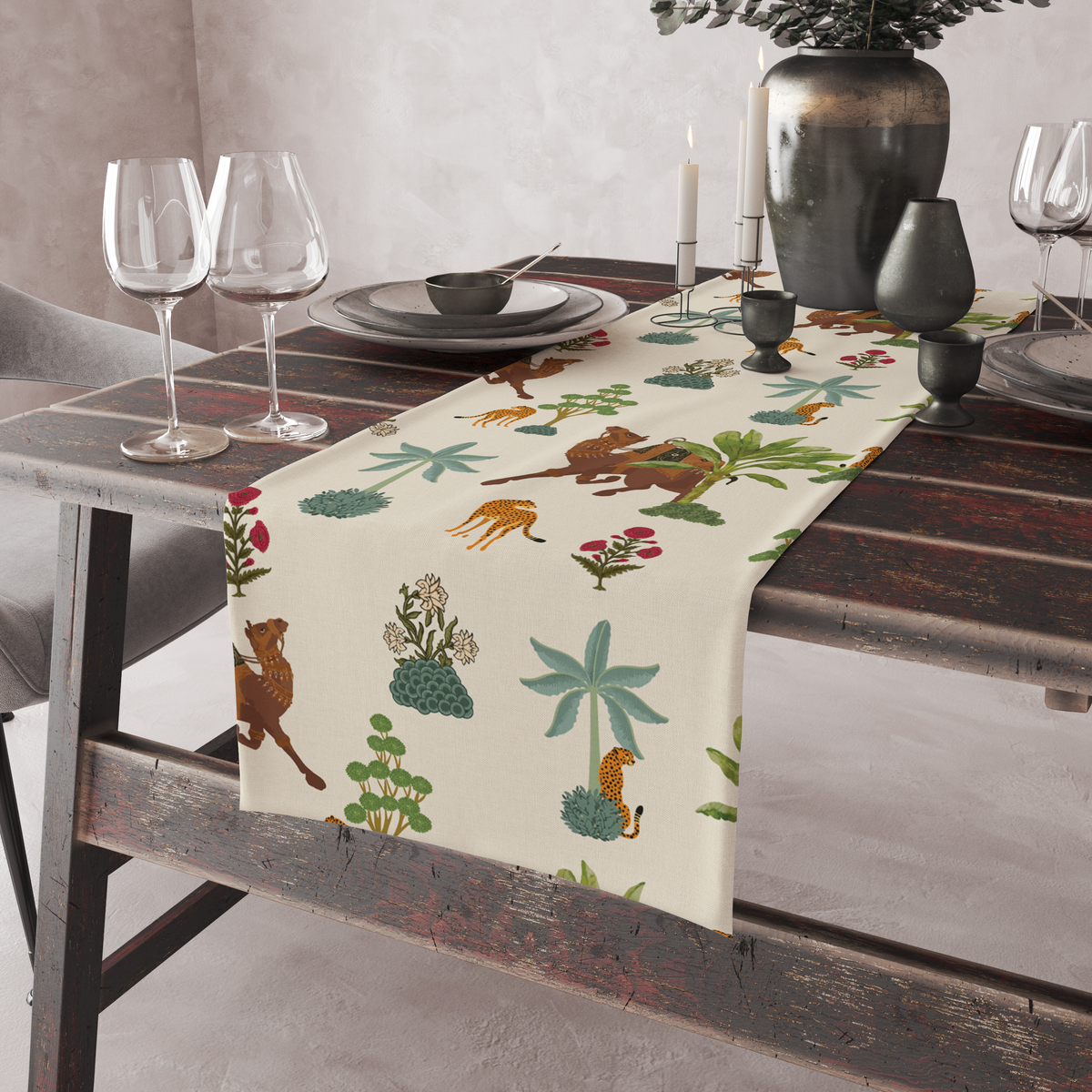 Cream table runner with camel, leopard, and palm-tree motifs, shown on a rustic table with wine glasses