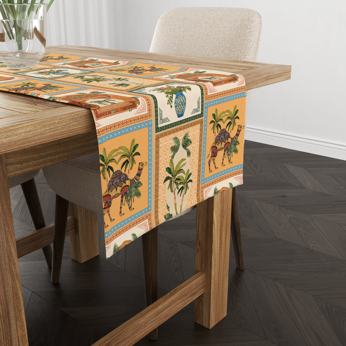 Checkered table runner with camel, palm-tree, jharokha-window, and floral vase motifs, shown from another angle on a wooden table with tableware