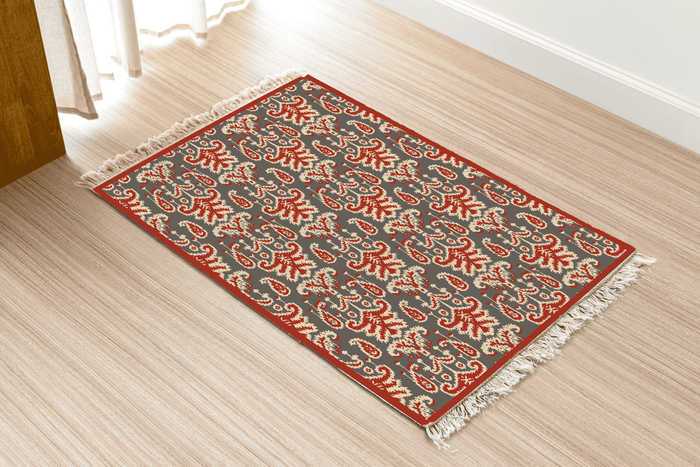 Angled view of the paisley-leaf Dhurrie rug on a wood floor near a curtained doorway