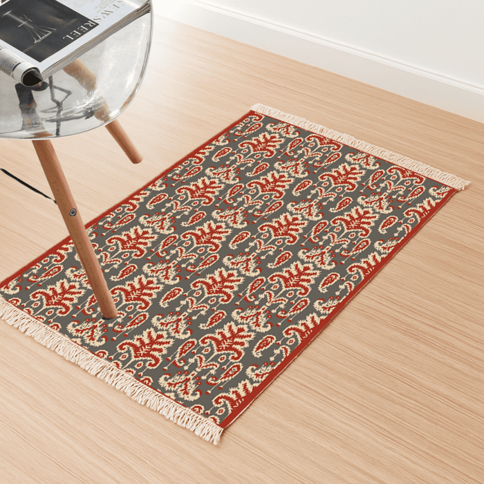 Angled view of the paisley-leaf Dhurrie rug on a light wood floor beside a chair