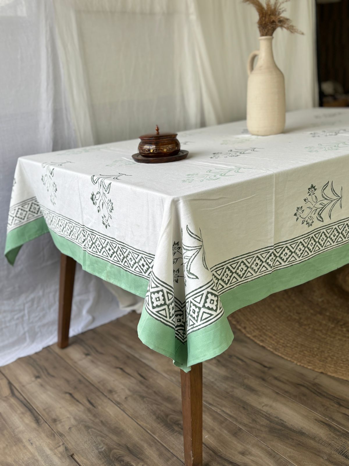 White tablecloth with a sage-green floral block print border and diamond lattice trim, shown close-up highlighting the block print border