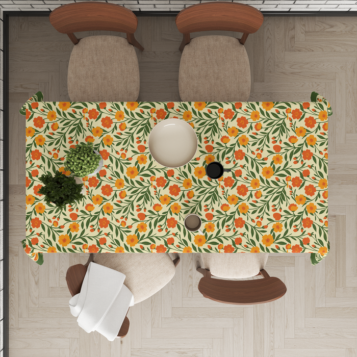 Cream tablecloth with a bright orange-and-yellow floral print, deep olive-green vine border, styled with tableware for a dining setting