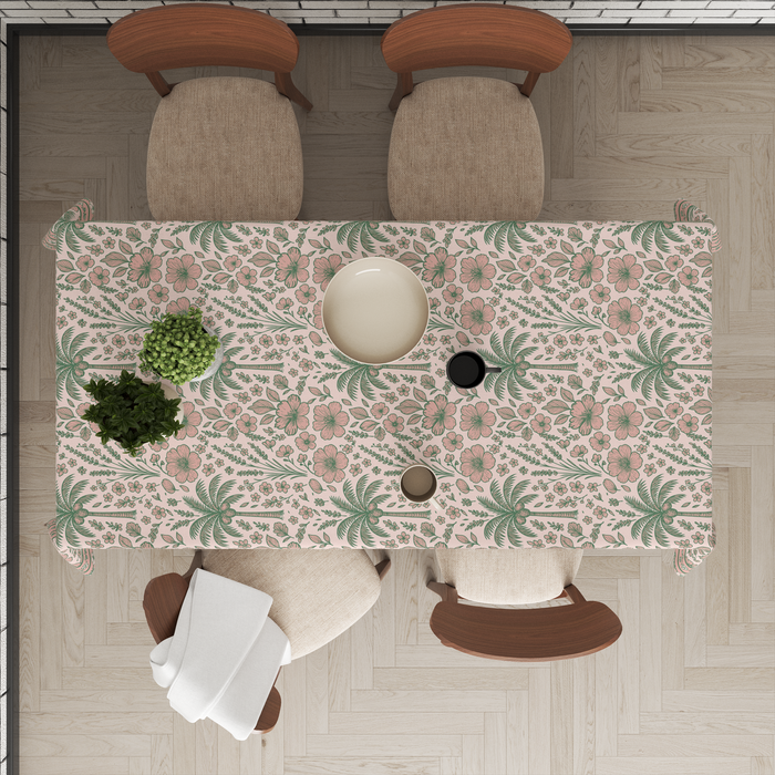 Blush-pink tablecloth with sage-green floral and palm-leaf motifs, matching striped border, styled with tableware for a dining setting