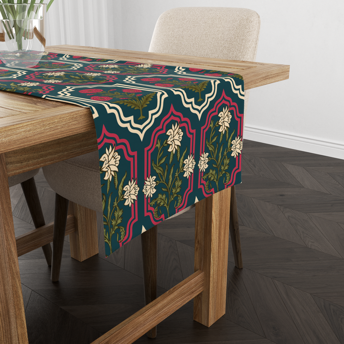 Deep teal table runner with ornate red and cream medallion frames and floral motifs, shown from another angle on a wooden table with tableware