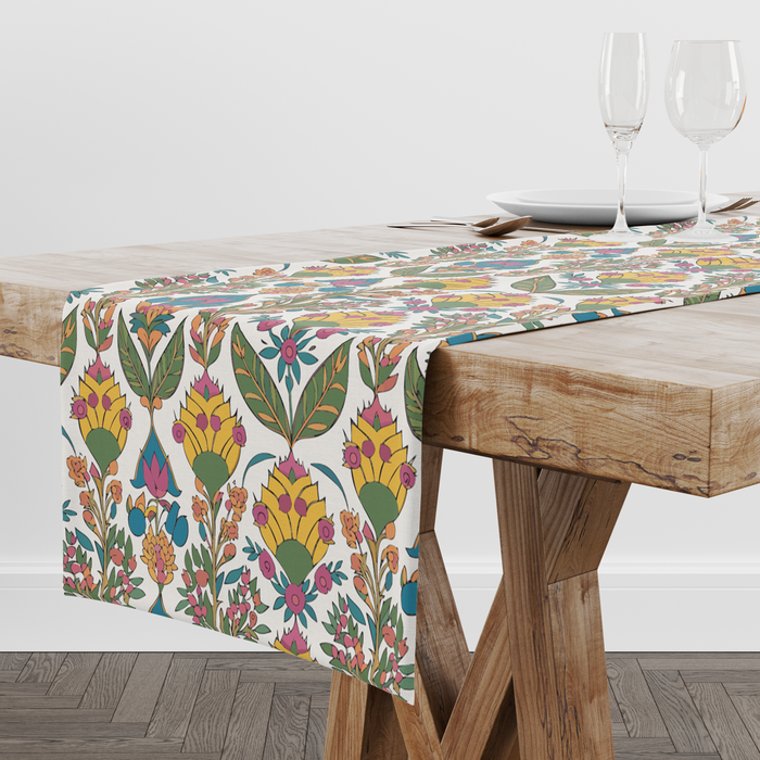 Cream table runner with a bold yellow blossom and green leaf print, pink and teal accents, styled with wine glasses and place settings