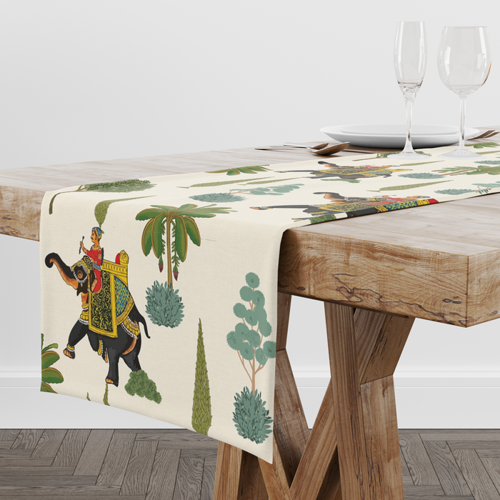 Cream table runner with decorated royal elephants, riders, and tree motifs, styled with wine glasses and place settings