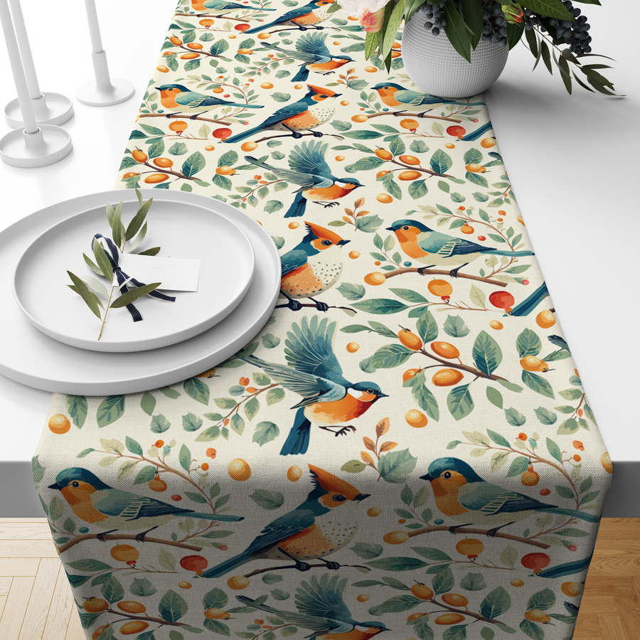 Cream table runner with blue and orange birds among branches with berries and citrus fruit, styled on a wooden dining table