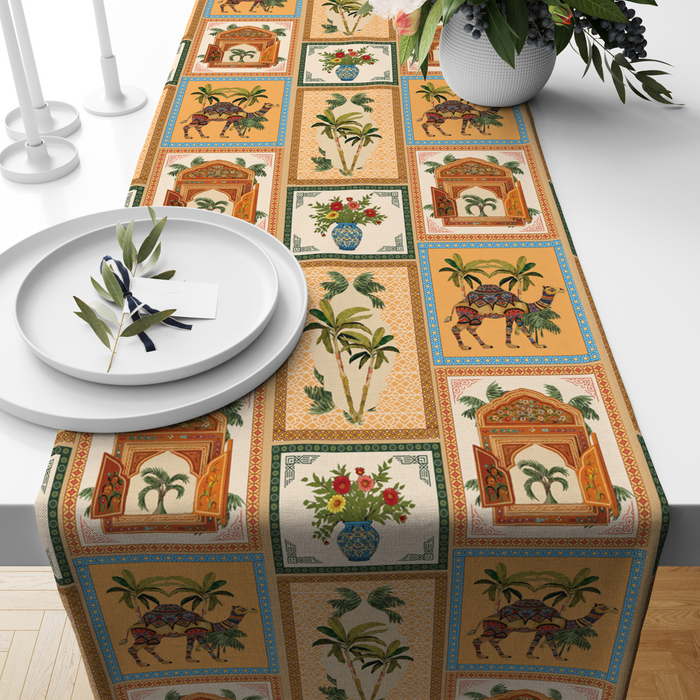 Checkered table runner with camel, palm-tree, jharokha-window, and floral vase motifs, styled on a wooden dining table