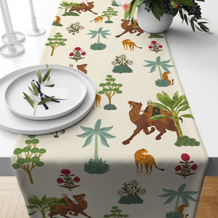 Cream table runner with camel, leopard, and palm-tree motifs, styled on a wooden dining table