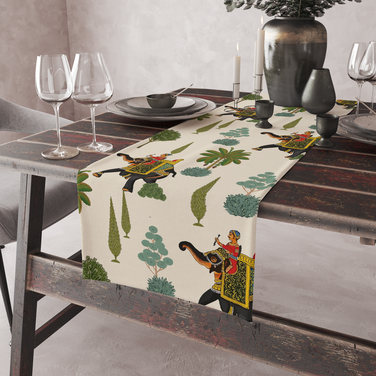 Cream table runner with decorated royal elephants, riders, and tree motifs, shown on a rustic table with wine glasses