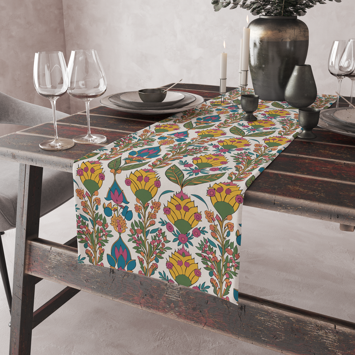 Cream table runner with a bold yellow blossom and green leaf print, pink and teal accents, shown on a rustic table with wine glasses