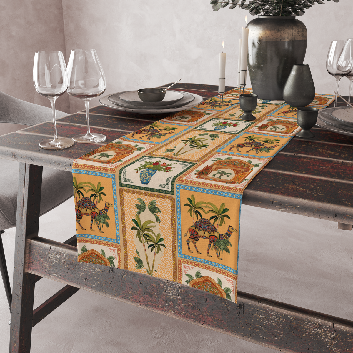 Checkered table runner with camel, palm-tree, jharokha-window, and floral vase motifs, shown on a rustic table with wine glasses