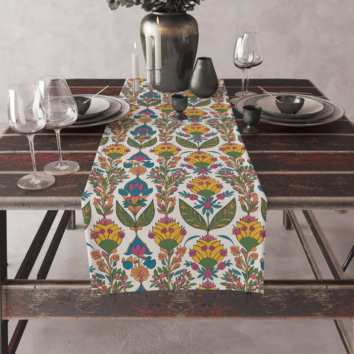 Cream table runner with a bold yellow blossom and green leaf print, pink and teal accents, set on a full dining table with candles