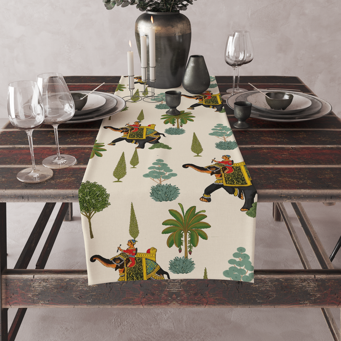 Cream table runner with decorated royal elephants, riders, and tree motifs, set on a full dining table with candles