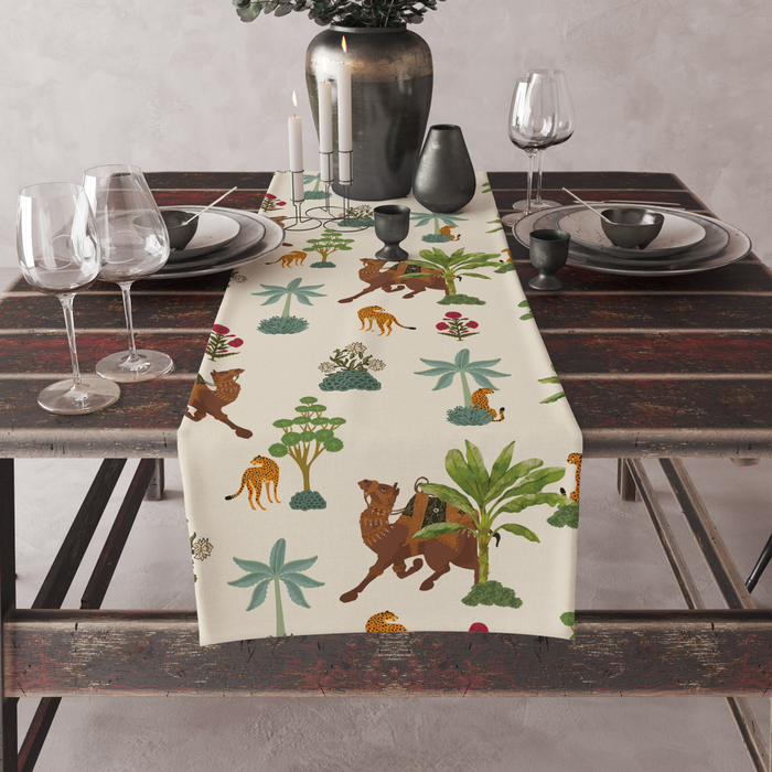Cream table runner with camel, leopard, and palm-tree motifs, set on a full dining table with candles