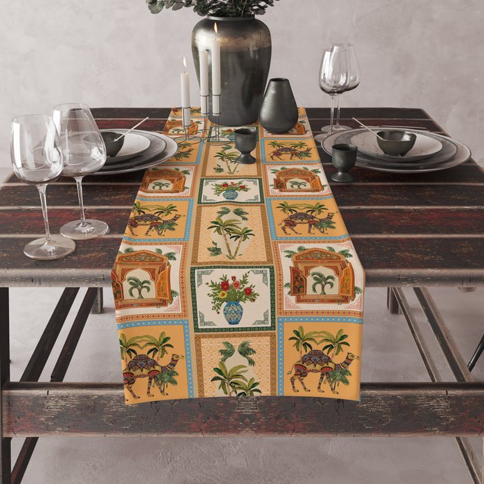 Checkered table runner with camel, palm-tree, jharokha-window, and floral vase motifs, set on a full dining table with candles