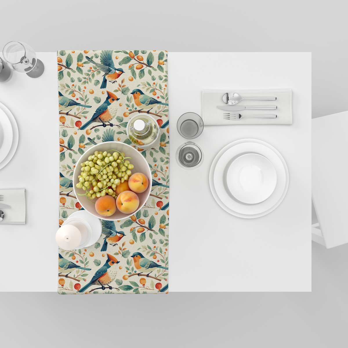 Cream table runner with blue and orange birds among branches with berries and citrus fruit, shown top-down with fruit bowl and tableware