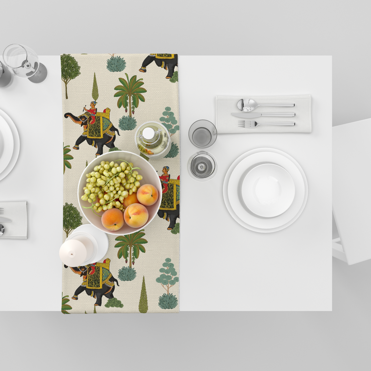 Cream table runner with decorated royal elephants, riders, and tree motifs, shown top-down with fruit bowl and tableware