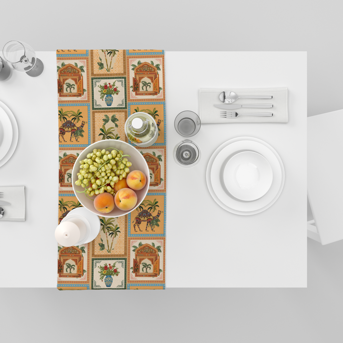 Checkered table runner with camel, palm-tree, jharokha-window, and floral vase motifs, shown top-down with fruit bowl and tableware