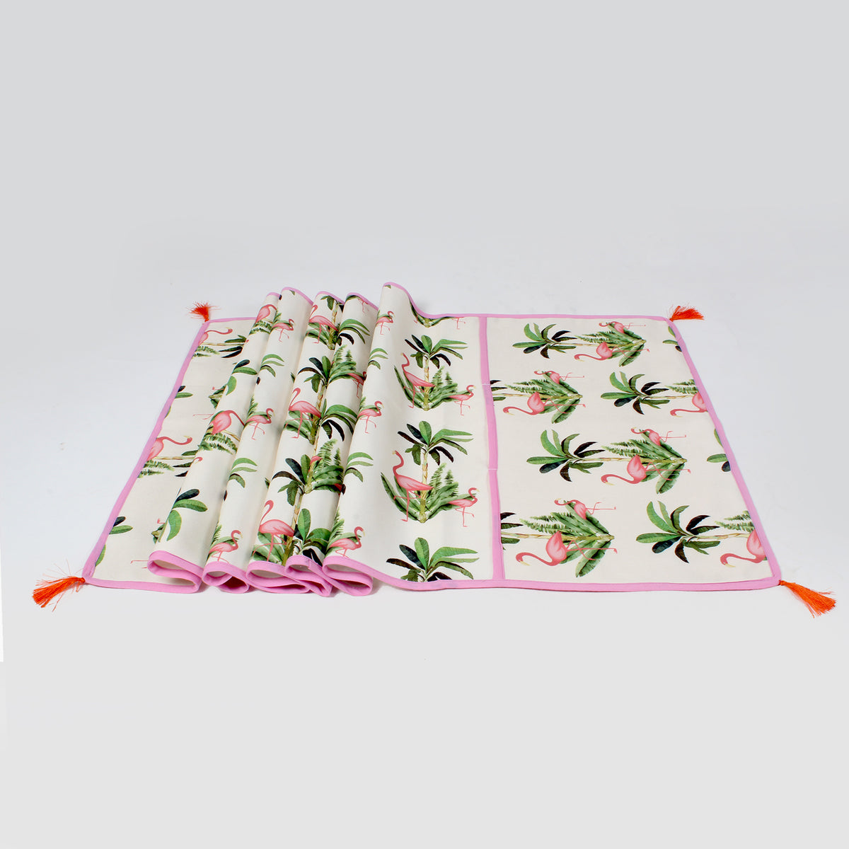 Folded flamingo and palm leaf print fridge cover with pink piping and orange tassels, shown flat