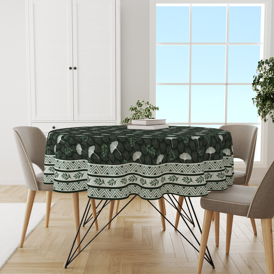 Dark green round tablecloth with tropical ginkgo leaf print and chevron border, on a dining table